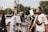 A group of people, some wearing traditional Muslim clothing and headbands reading 'Free Palestine,' participate in a protest or rally. They hold signs with messages supporting Palestine. The scene is outdoors, with trees and vehicles visible in the background.