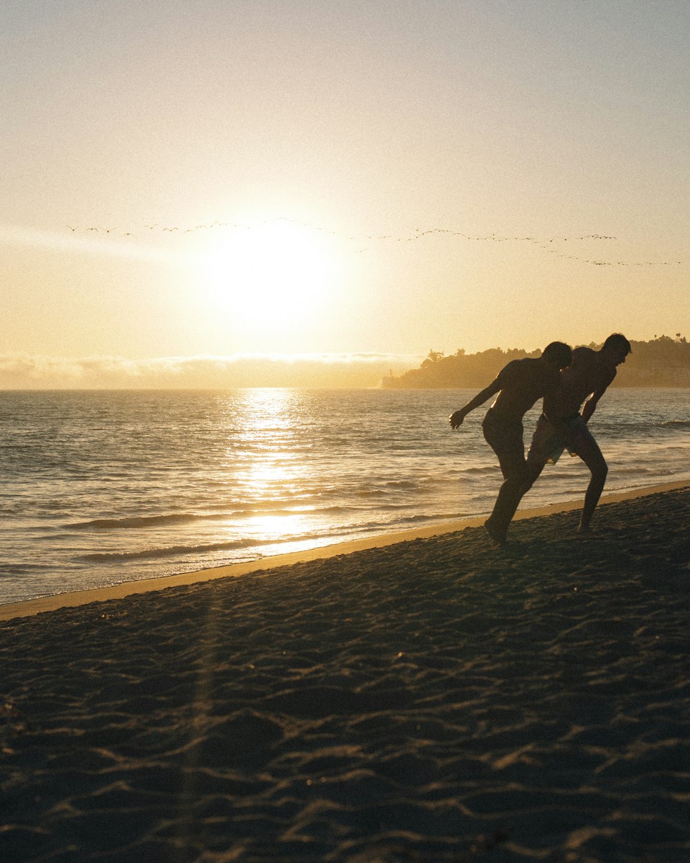 two people playing frisbee on the beach at sunset