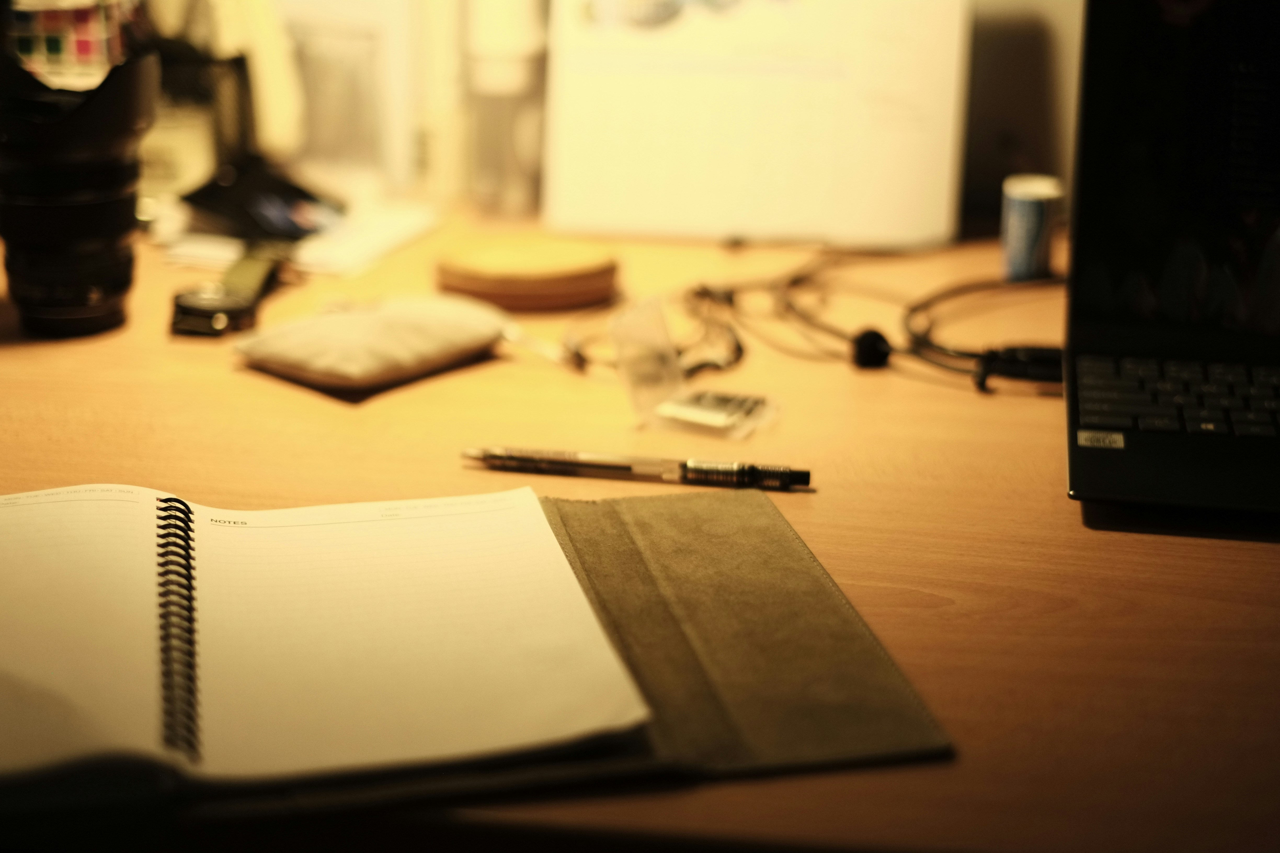 Notebook with organized notes and pen beside laptop, bright workspace, warm natural light