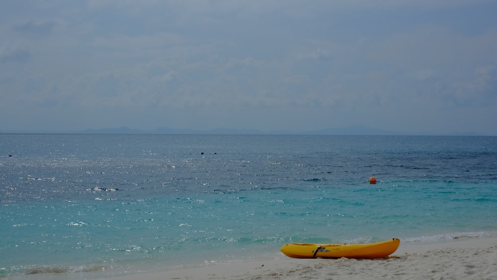 a yellow kayak sitting on the beach next to the ocean