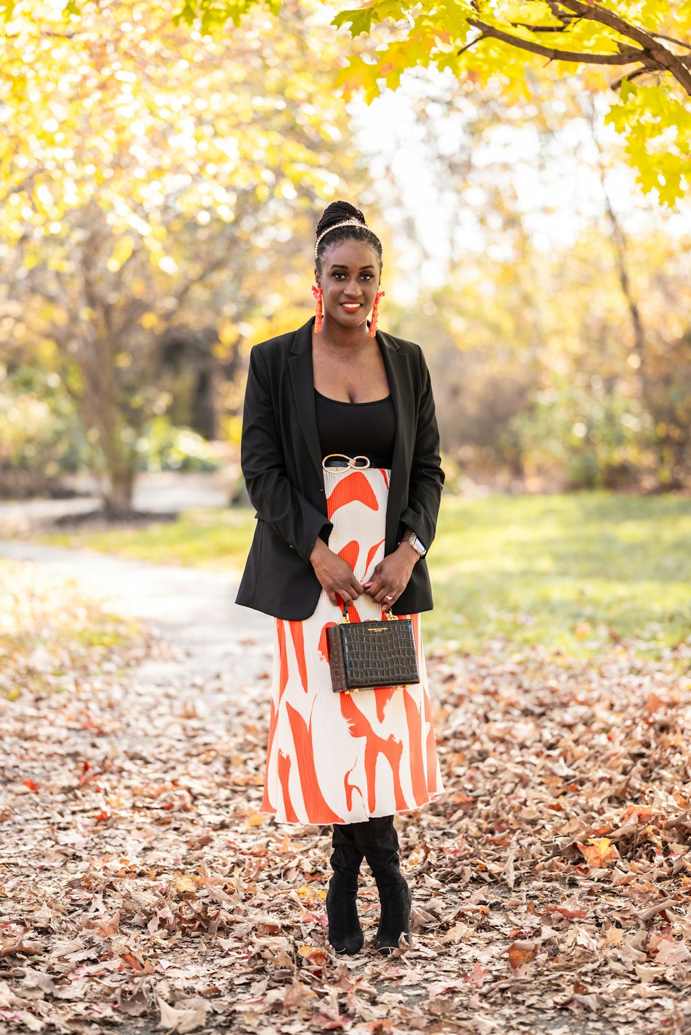 a woman standing in leaves holding a purse