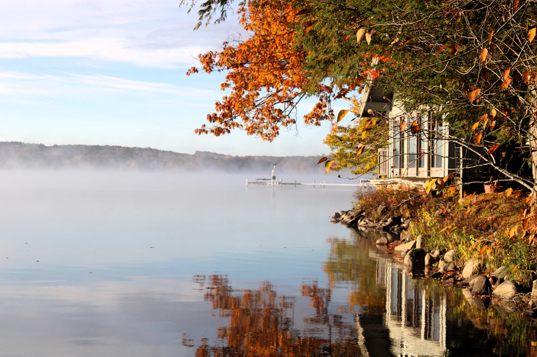 Lakeside home among autumn trees on a misty morning