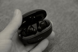 a hand holding a pair of black earbuds