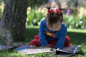 a little girl sitting in the grass reading a book