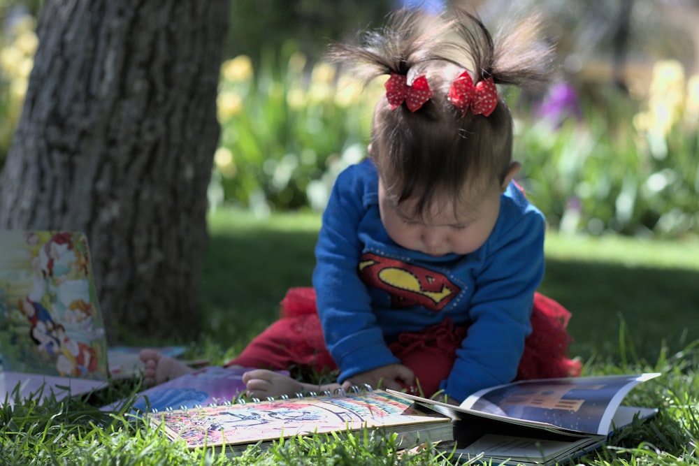 a little girl sitting in the grass reading a book