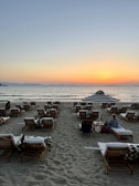 A serene beach scene with travelers relaxing on lounge chairs during sunset.