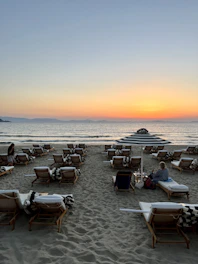 A serene beach sunset with a couple relaxing on lounge chairs.