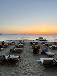 A serene beach sunset with a couple relaxing on lounge chairs.