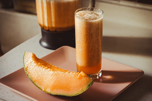 A glass of orange juice next to a sliced melon