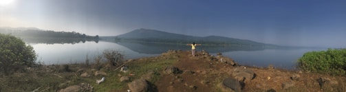 A welcoming fitness coach smiling and ready to assist by a serene lake backdrop.
