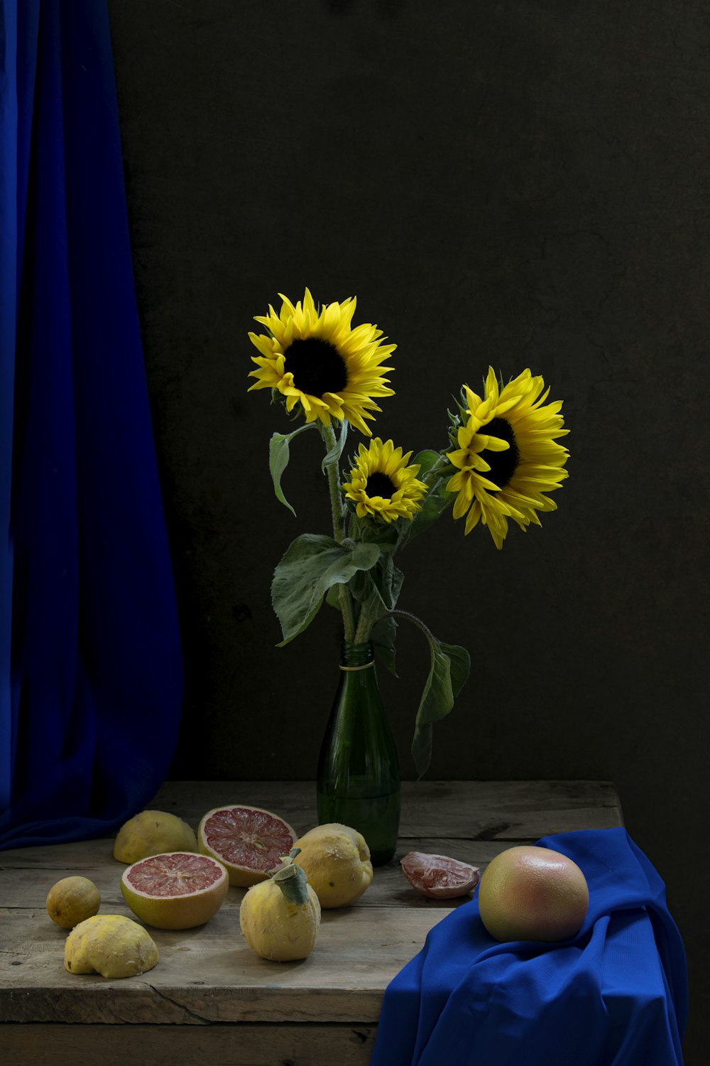 a vase of sunflowers and other fruit on a table