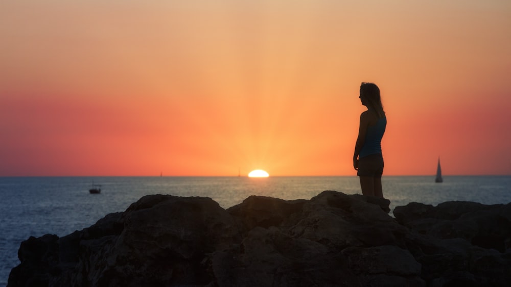 a woman standing on a rock watching the sun set