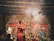 A traditional religious setup featuring intricately decorated statues of deities, with figures in ceremonial attire performing a ritual. Smoke rises amidst the vibrant decorations, adding a mystical atmosphere to the scene.