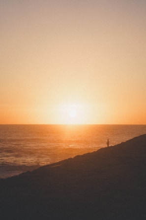 Solo traveler admiring a stunning sunset over the ocean, thanks to Carleone Neres