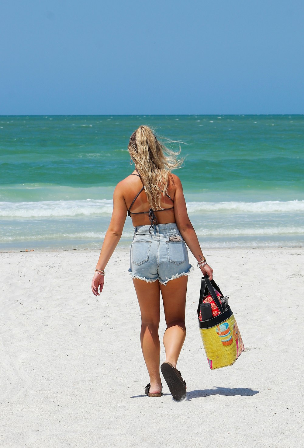 a woman walking on the beach carrying a bag