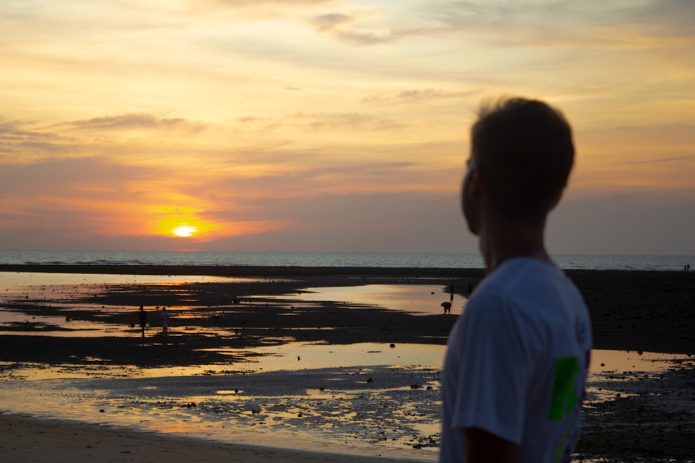 a man standing on a beach watching the sun set