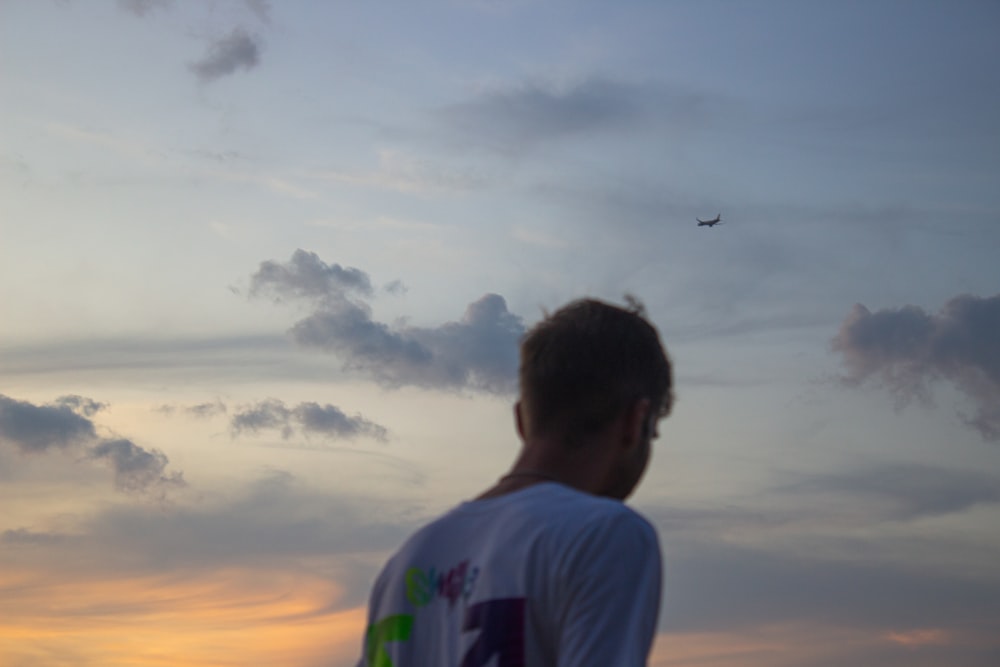 a man looking at a plane flying in the sky