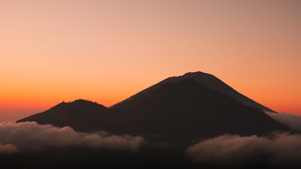 ein wolkenverhangener Berg mit einem Sonnenuntergang im Hintergrund