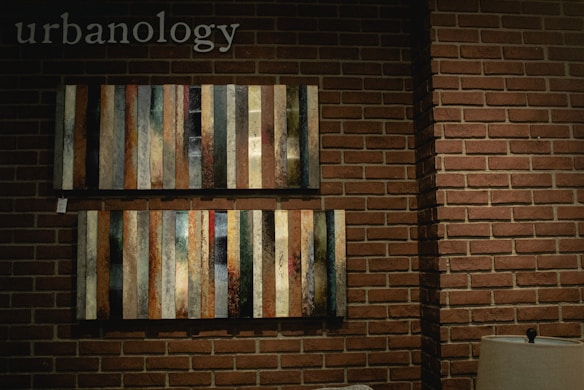Vertical striped artwork is displayed against a brick wall, with a small lamp on the side. The word 'urbanology' is visible at the top left.
