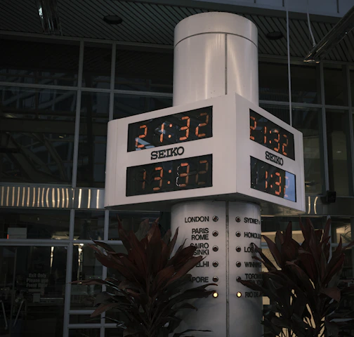 A sleek, minimalist digital clock display showing multiple world cities' times on a soft blue background.