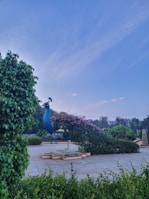 An outdoor garden scene featuring a graceful fiberglass peacock sculpture surrounded by lush greenery.