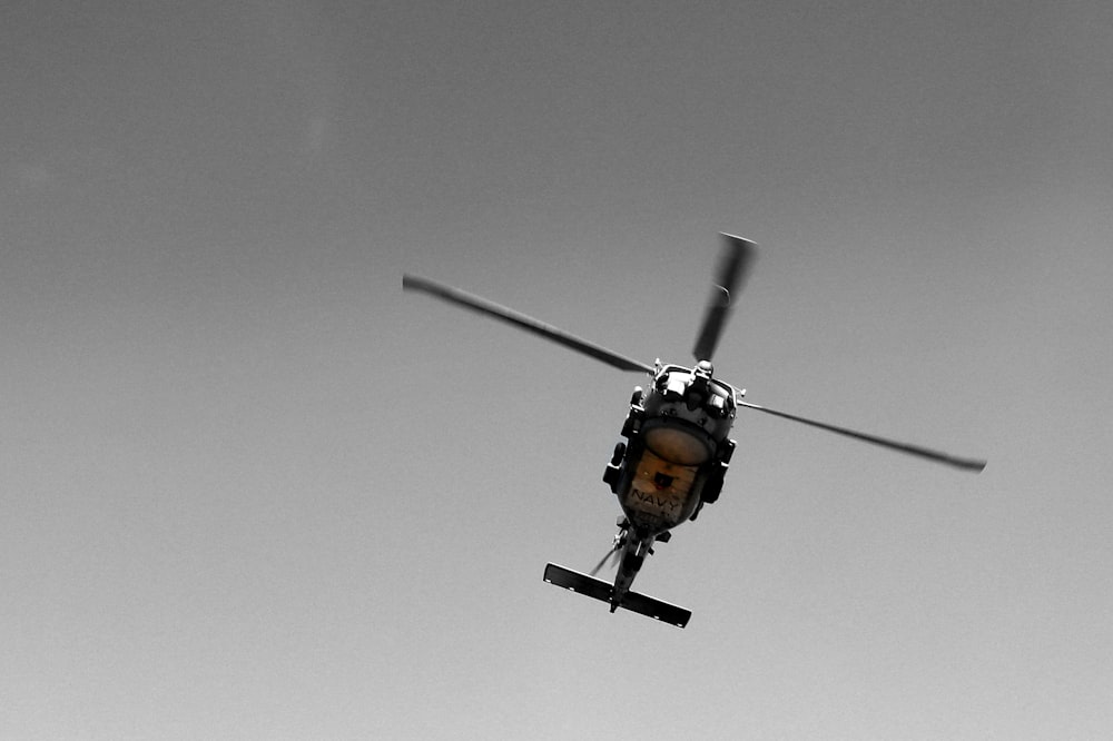 a black and white photo of a helicopter flying in the sky