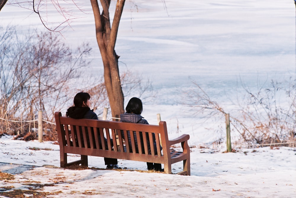 two people sitting on a bench in the snow