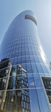 Close-up of a sleek glass facade reflecting a city skyline under a clear blue sky.
