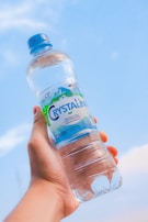 Hands holding a chilled 500ml Água Mineral Croatá bottle outdoors on a sunny day.
