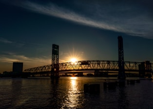 the sun is setting over a bridge over a body of water