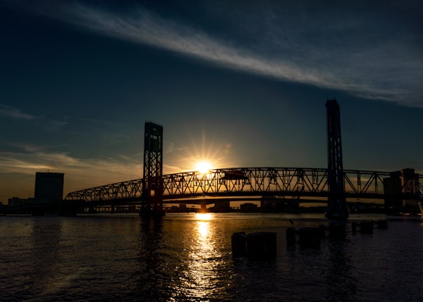 the sun is setting over a bridge over a body of water