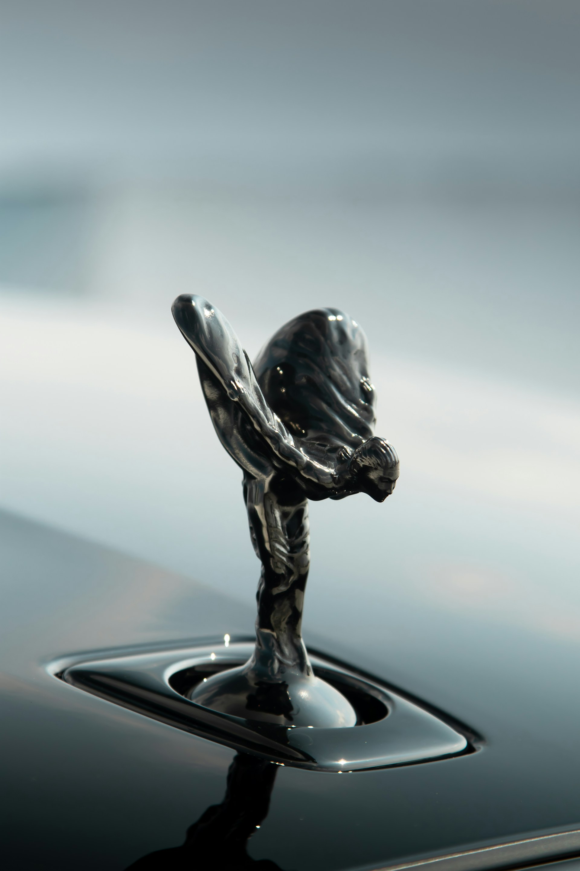 A metallic sculpture shaped like a winged figure is mounted on a sleek, glossy surface. The design is intricately detailed, capturing elegance and movement in the figure's flowing lines.