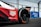 A close-up view of the rear wheel of a race car, prominently displaying the TAG Heuer logo and the word 'electric' on the side. The car has sleek, aerodynamic bodywork with visible branding. The wheel features Hankook tires with colorful markings. There is a wire fence and a blue advertisement board in the background.