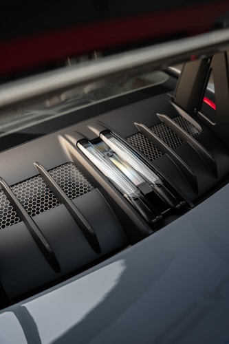 A close-up of a high-performance car engine cover featuring vents and hexagonal mesh, showcasing intricate detailing and modern design elements.
