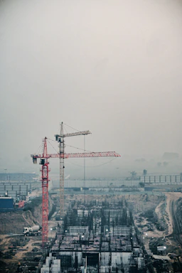 A professional handshake between two engineers at a construction site with cranes and building structures in the background.