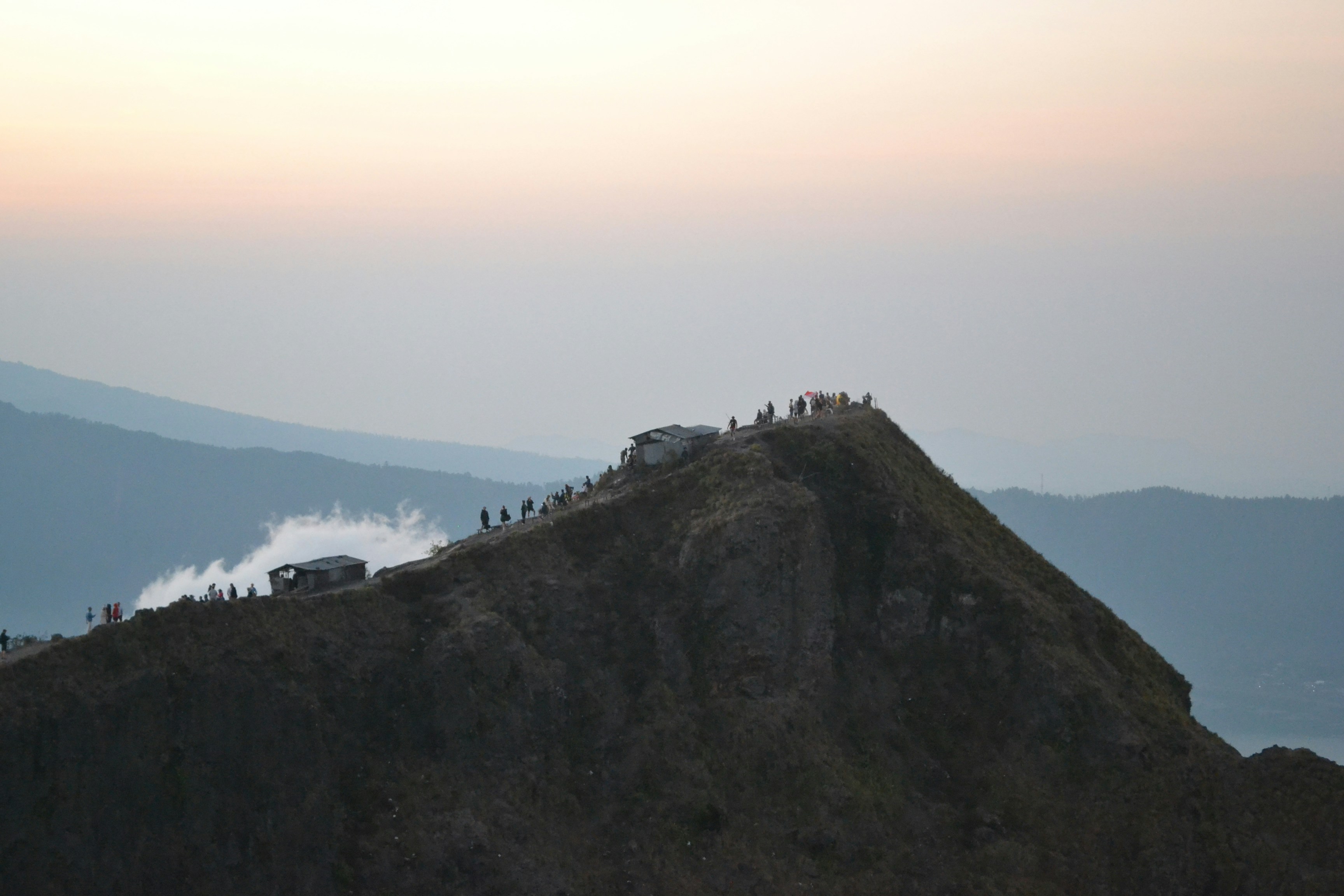 Climbers at Uhuru Peak summit sign at dawn, pink sky, vast crater rim behind them
