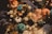 A close-up of a decorative arrangement featuring an assortment of dried flowers and plants. The composition includes sunflowers, textured blue and orange elements, and soft, fuzzy spheres reminiscent of dried cotton flowers. Additional foliage contributes to the earthy, rustic appearance.
