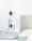 A dropper bottle labeled 'nuface Nu Glow' is positioned on a textured white stone surface with additional stone blocks in the background. The bottle contains a skin serum with a clear glass body and a metallic cap.