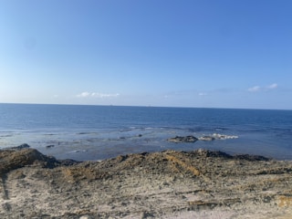 A researcher collecting sediment samples along a rocky shoreline under a clear blue sky.