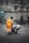 A worker in bright orange reflective clothing pushes a cart loaded with garbage bags down a city street. The background features bicycles lined up against a railing, pedestrians walking by, and large buildings with stone facades. A digital billboard and a no parking sign are visible, adding to the urban setting.
