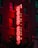 A neon sign with the words 'Hong Kong' in bright red letters is mounted vertically on the side of a brick building. The glowing sign is outlined by small white bulbs, which add extra illumination. Several windows are visible in the building, with some lights reflecting in them. The scene is set in the evening, creating a vibrant and slightly nostalgic urban atmosphere.