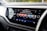 A car dashboard displays a digital infotainment system screen. The screen shows a radio interface with various channels like BBC R1, BBC R2, and BBC R6M. The current station playing is Capital DANCE with a song by Tall Paul. The interface includes options for radio, media, phone, and voice control, and the current time is displayed.