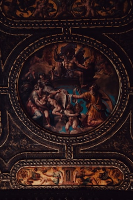 A richly detailed and dramatic classical artwork featuring mythological figures arranged in an ornate circular frame. The scene includes dynamic poses, flowing garments, and intricate detailing, all set against a vividly colored backdrop. The craftsmanship of the gold embellishments highlights the grandeur of the composition.