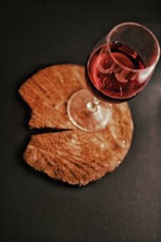 A lively glass of red wine with a playful splash on a rustic wooden table, surrounded by casual wine accessories.