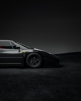 A sleek, black sports car with a low profile, displaying a logo on its side and detailed wheels. The setting is a dimly lit environment with a soft gradient background.