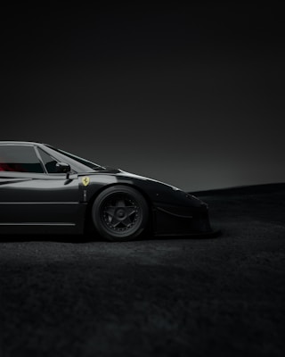 A sleek, black sports car with a low profile, displaying a logo on its side and detailed wheels. The setting is a dimly lit environment with a soft gradient background.