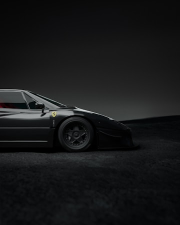 A sleek, black sports car with a low profile, displaying a logo on its side and detailed wheels. The setting is a dimly lit environment with a soft gradient background.