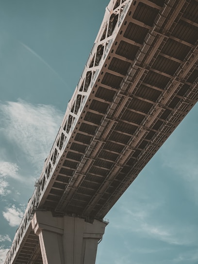 Photo of a confident pipe welder working on an industrial bridge structure under a clear sky.