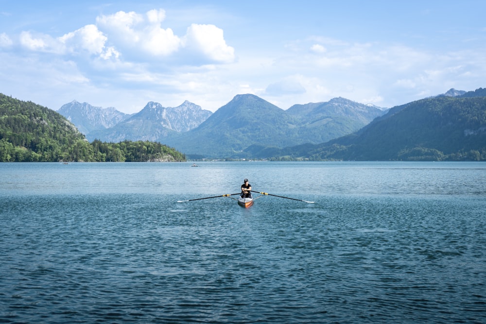 a person rowing a boat on a lake with mountains in the background