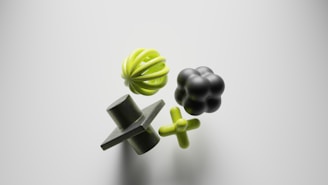 Four abstract geometric shapes float against a light background. The objects include a green sphere with curved ridges, a black rounded shape resembling a cluster of spheres, a green plus-shaped figure, and a dark green cone with a square intersecting its middle.